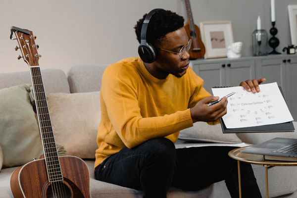Homem negro segurando uma folha com anotações musicais, dando aula de música online